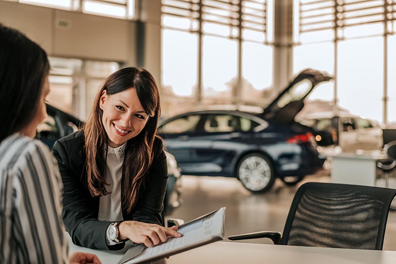 Two woman finalizing car purchase by reviewing paperwork. 